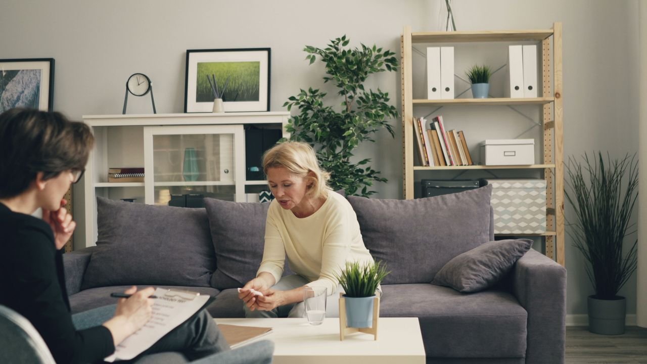 A woman consults with a therapist in a modern, cozy home setting, focusing on mental health.