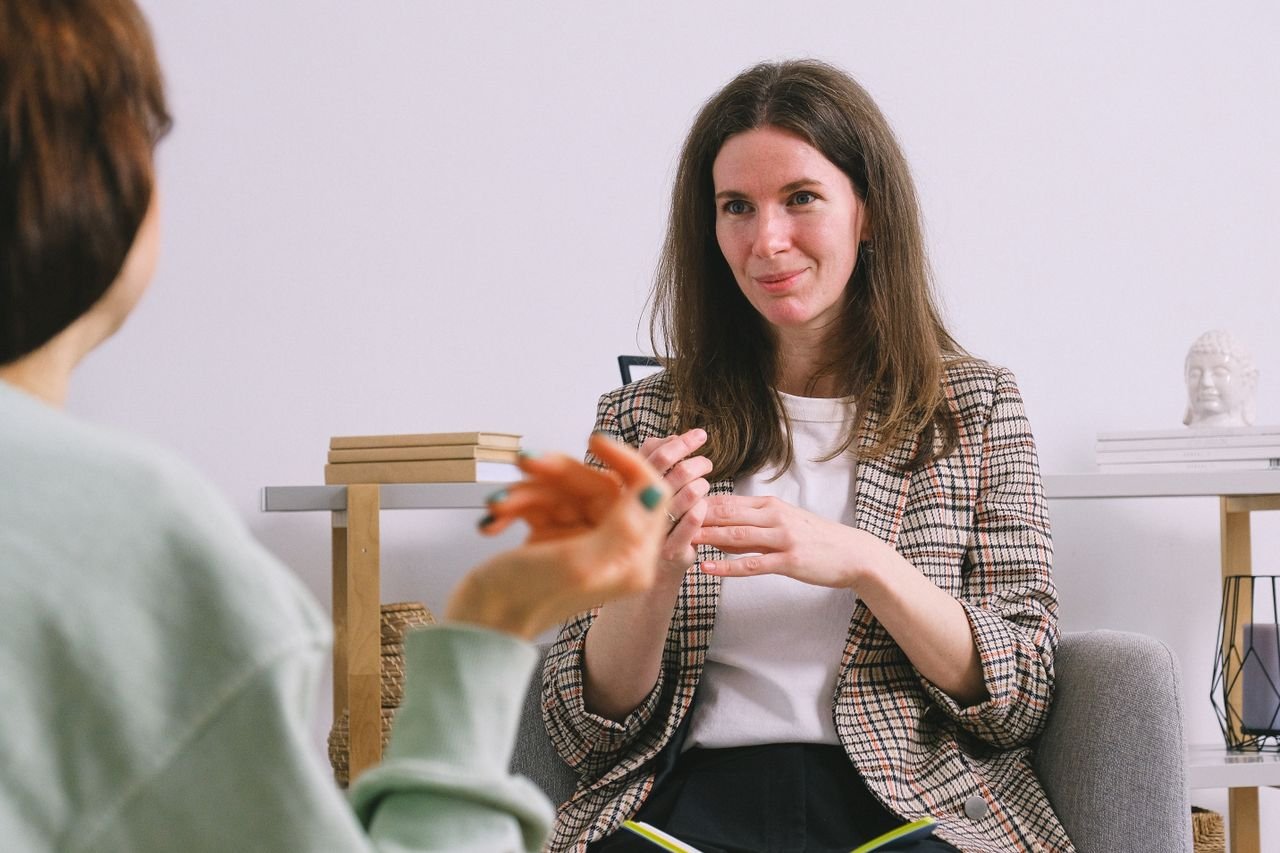 Sincere female counselor speaking with crop unrecognizable woman gesticulating during psychological session on white background